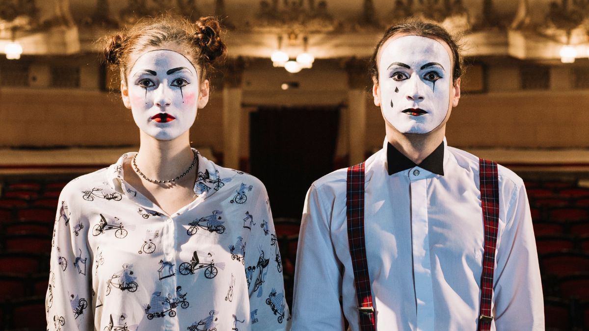 Duas pessoas com maquiagem e luvas de mímico em pé em um grande teatro vazio. no Dia Mundial do Teatro