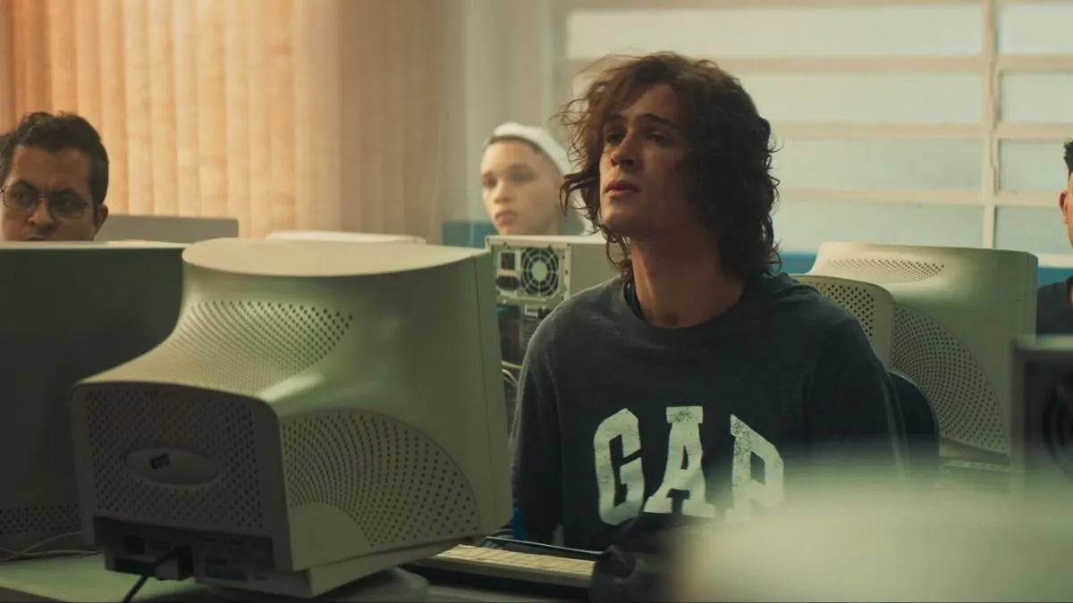 foto do personagem de João Guilherme no filme "O Rei da Internet"; ele está em uma sala com vários computadores olhando para frente