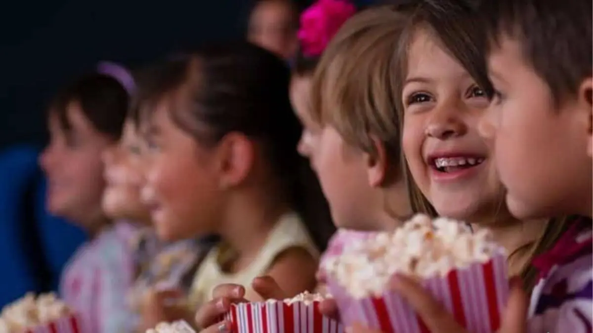 foto de crianças com pipoca na mao e sorrindo ilustrando estar em uma sala de cinema