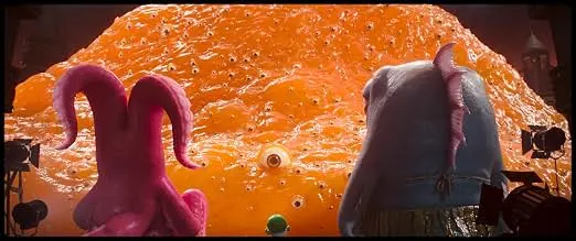 Foto de dois monstros em primeiro plado de costas, olhando uma criatura gigante da cor alaranjada com vários olhos, em referência ao filme A Grande Bolha em Minions & Monstros