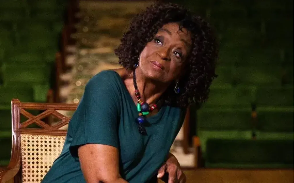 Imagem de Léa Garcia sentada com vestido verde e cabelos soltos olahndo para cima