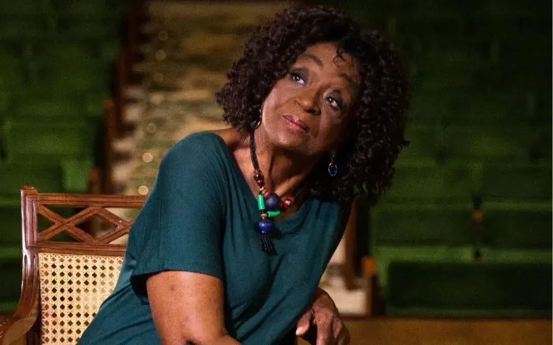 Imagem de Léa Garcia sentada com vestido verde e cabelos soltos olahndo para cima