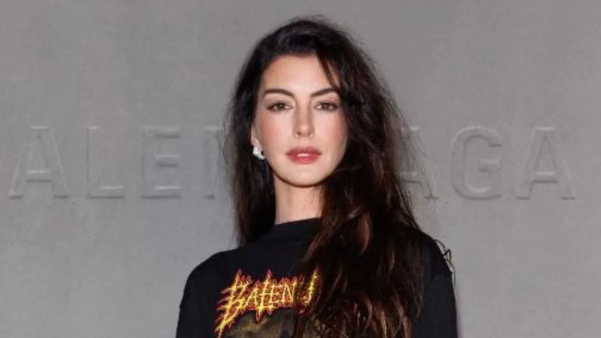 Anne Hathaway com cabelos soltos e blusa preta olhando para frente para a foto